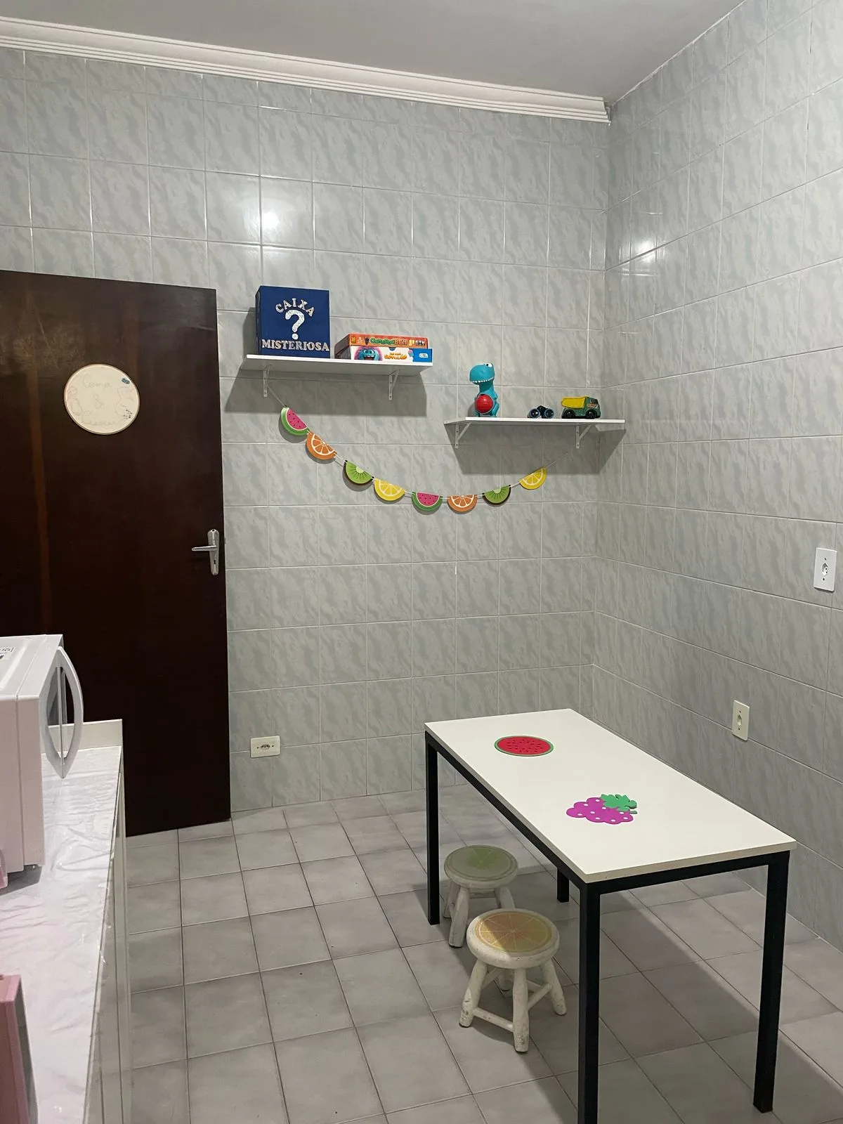 Mesa baixa com banquinhos e varal de frutas de feltro na parede da cozinha
